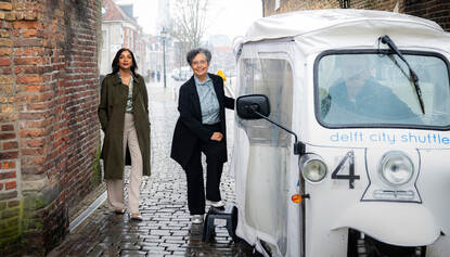 Safiela Chand en Janine Ahlers, poserend naast een Delft City Shuttle bij de Oostpoort, één van de stadspoorten in Delft