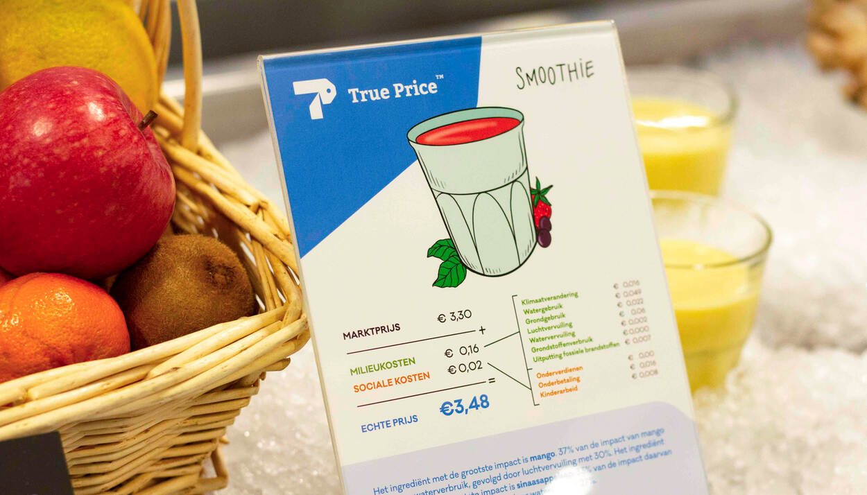 Informatiebord met prijzen van een smoothie. De marktprijs van een smoothie bedraagt € 3,30, de echte prijs, dus inclusief milieukosten en sociale kosten, bedraagt € 3,48.