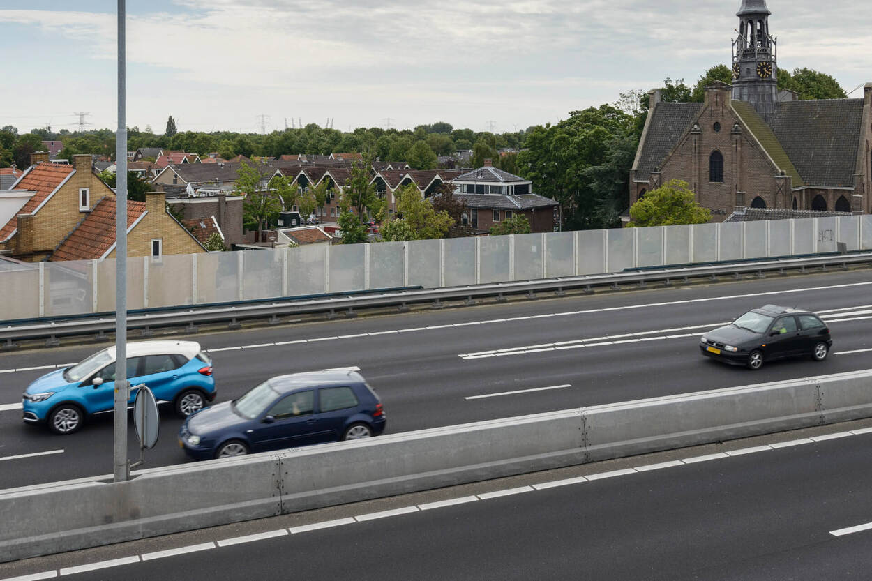 Auto's op de snelweg rijden langs een geluidscherm, met daarachter een woonwijk.