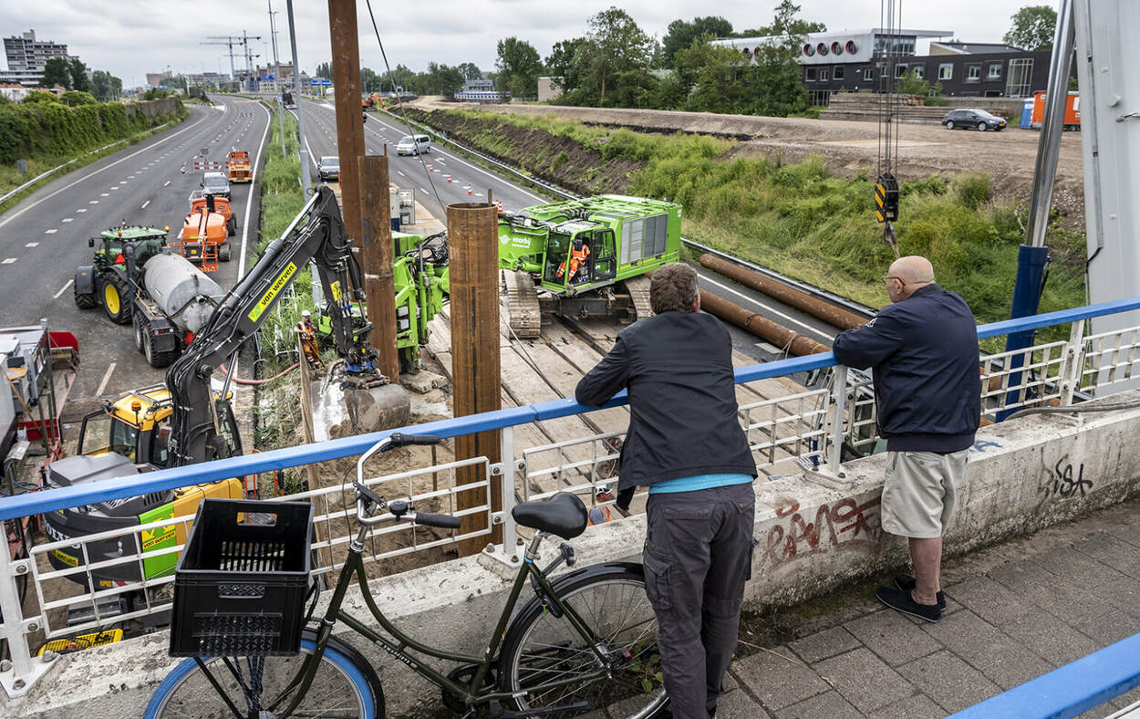 Voorbijgangers kijken toe bij de werkzaamheden vanaf een tijdelijke fietsbrug over de A9 in Amstelveen