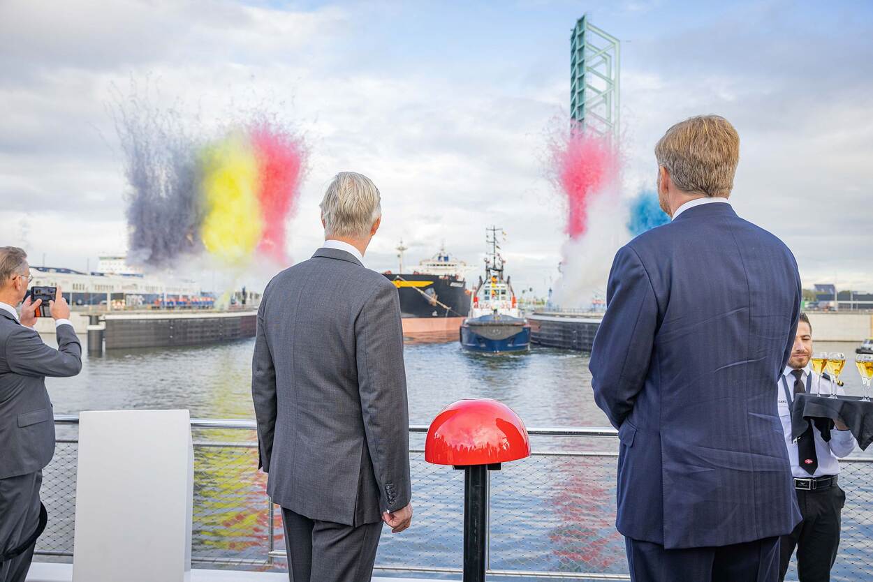 Koning Filip en koning Willem-Alexander op de rug gezien terwijl zij toekijken hoe het eerste schip door de Nieuwe Sluis vaart. Op de achtergrond vuurwerk in de kleuren van de Belgische en Nederlandse vlag.