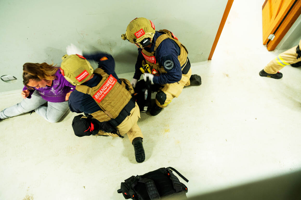 Twee brandweermannen gehurkt bij vrouw tijdens oefening