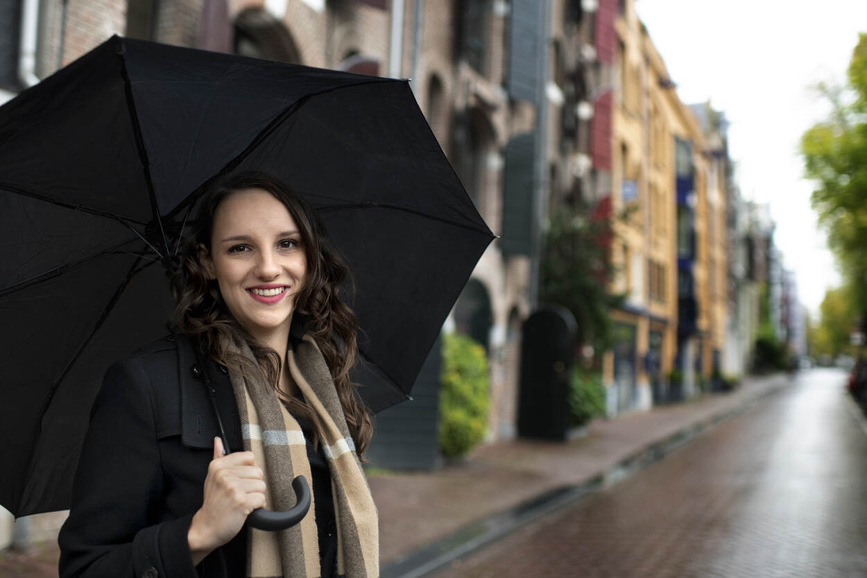 Portretfoto van Roos Nieuwendijk buiten in de regen onder een zwarte paraplu