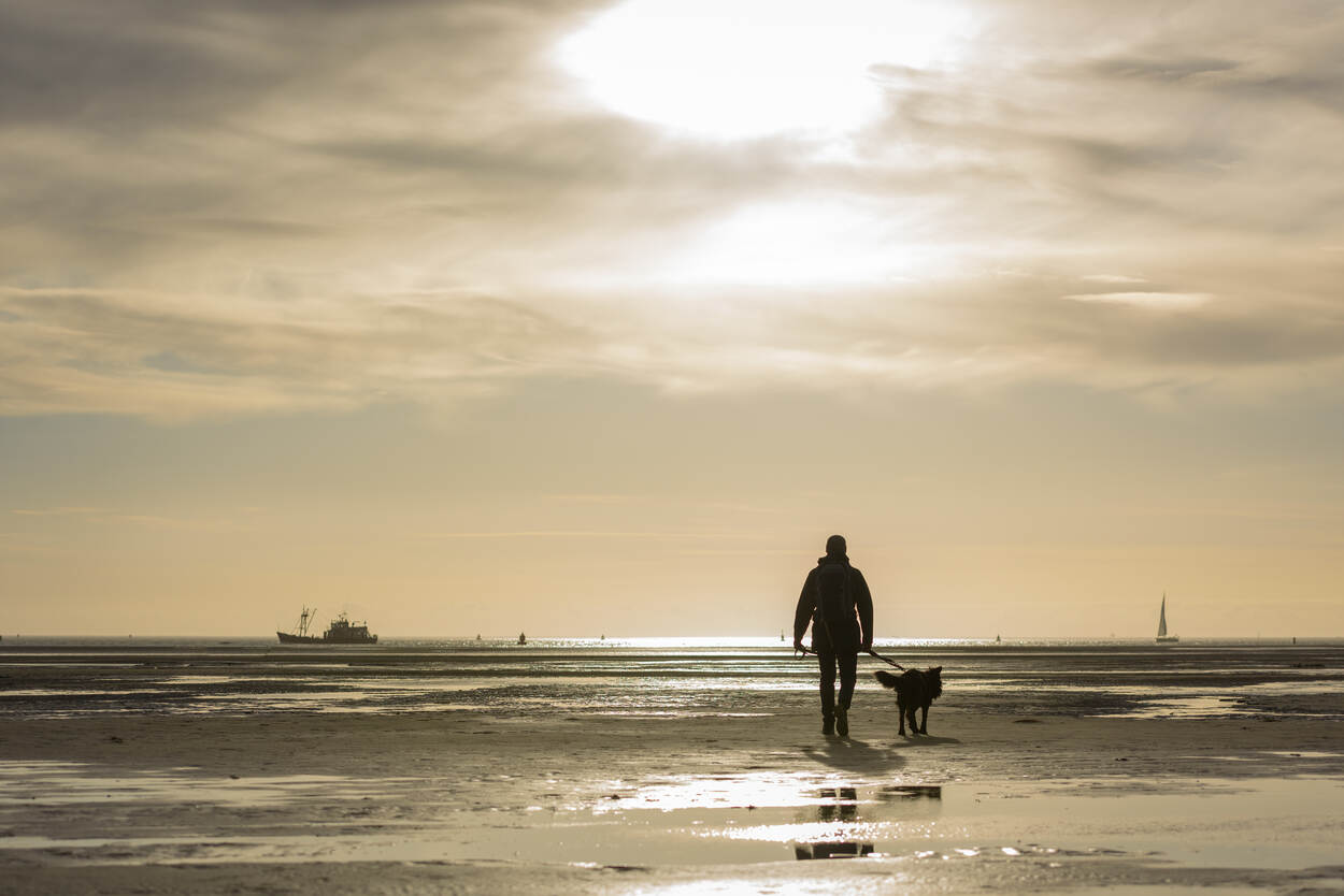 Foto in sepia van Adriaan Brouwer met zijn zwarte hond op het strand van Terschelling