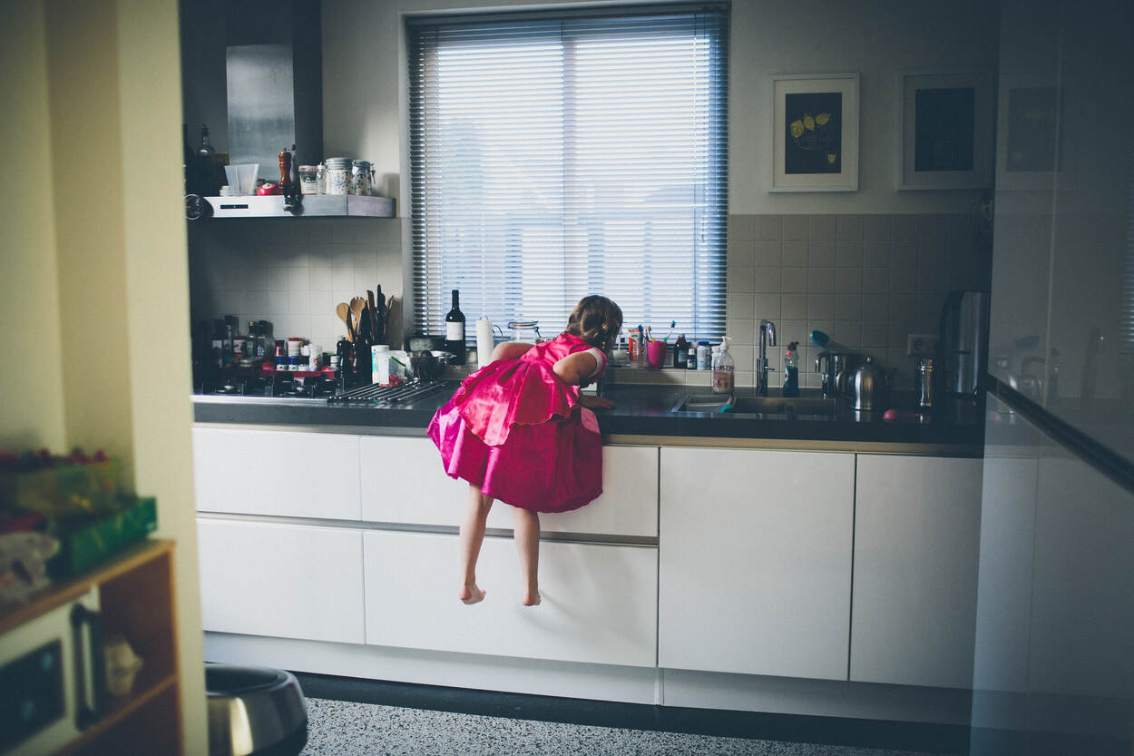 Klein meisje in een felroze jurk hangt over de gootsteen in de keuken