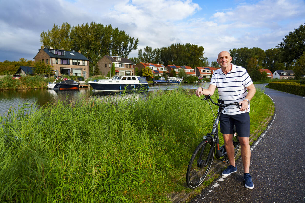 Foto van Theo van Wijnen met zijn fiets aan de hand buiten in een groene omgeving met huizen op de actergrond
