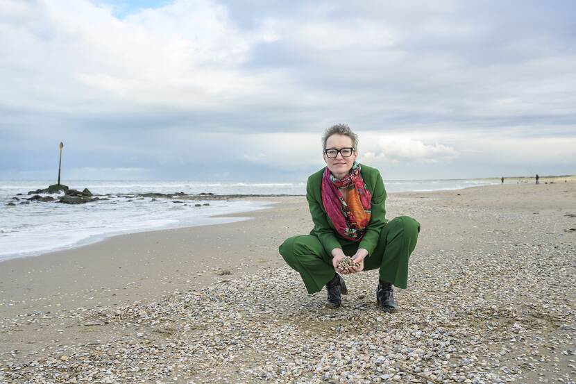 Annemiek Roeling gehurkt op het strand met een handvol schelpen