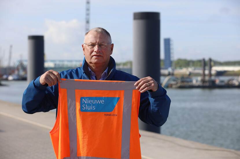 Projectleider Eric Marteijn staat op de brug over de nieuwe sluis, met een veiligheidshesje in zijn handen met op de rug de tekst Nieuwe Sluis