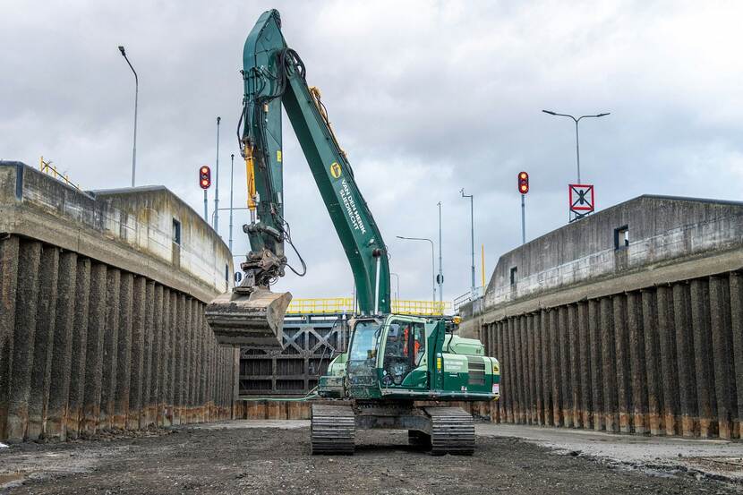 Graafmachine op rupsbanden rijdt over de bodem van een sluis bij Born.