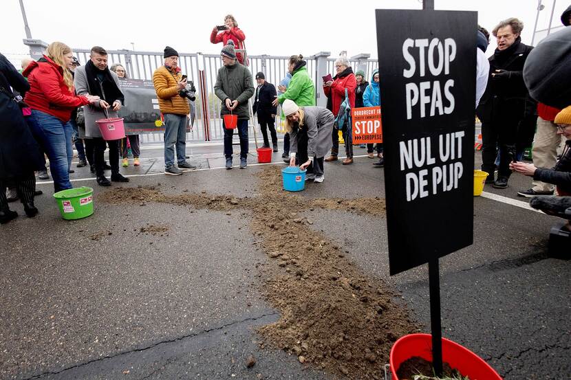Demonstranten maken met door PFAS vervuilde grond een kruis voor de poort van Chemours in Dordrecht met een protestbord met de tekst: PFAS nul uit de pijp