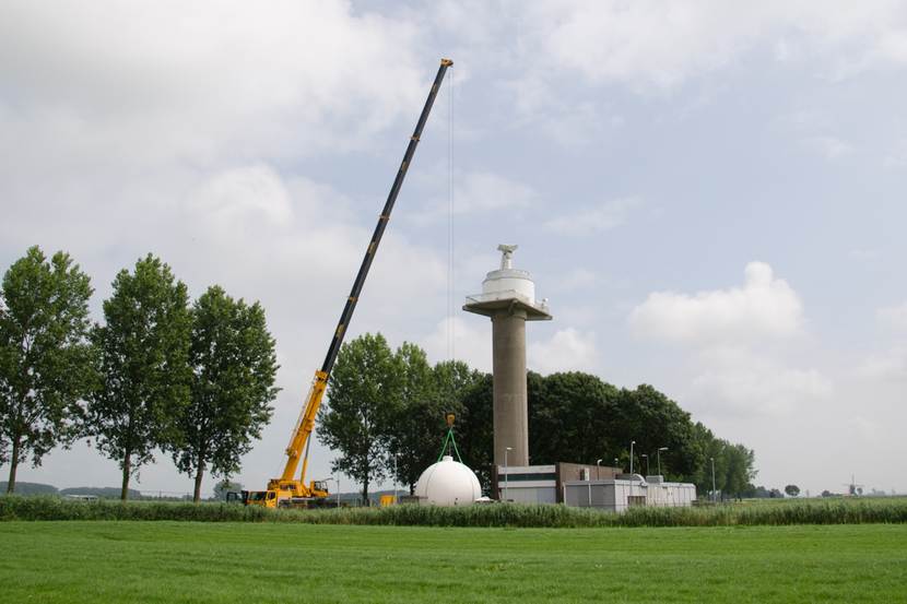 Foto van een hijskraan naast de nieuwe radartoren in Herwijnen, die de nieuwe radarbol op de toren gaat hijsen
