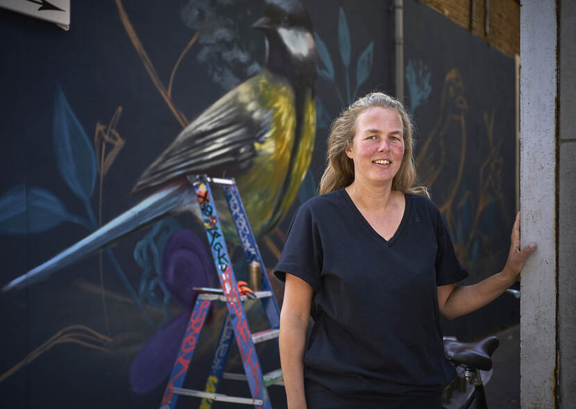 Joy Falkena, een jogerenwerker met op de achtergrond een muurschildering van een vogel