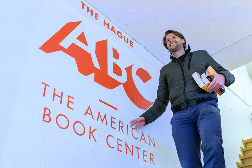 Drian van der Woude bij het logo van ABC - the America Book Centre
