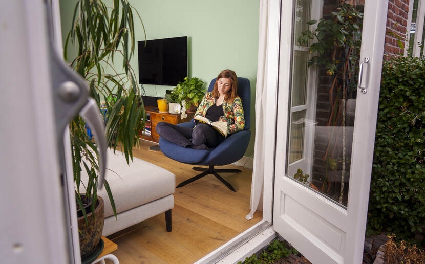 Zinzi Aben zit in haar woonkamer met gekruiste benen in een draaistoel bij opengeslagen deuren richting de tuin