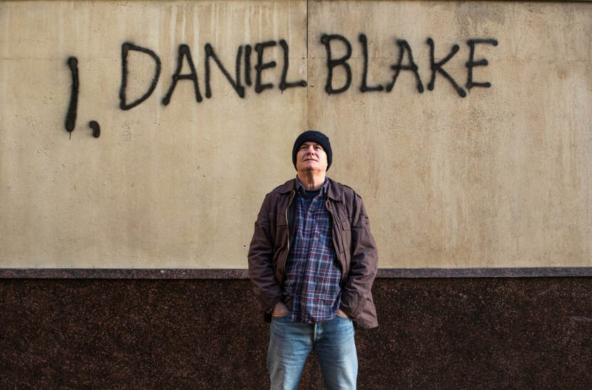Screenshot waarin Daniel Blake voor een muur staat met daarin in graffiti: I, Daniel Blake