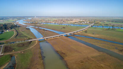 Dronefoto van het projectgebied Hoogwatergeul Ooijen-Wanssum, met de hoogwatergeul parallel aan de Maas, en een nieuwe brug over het gebied