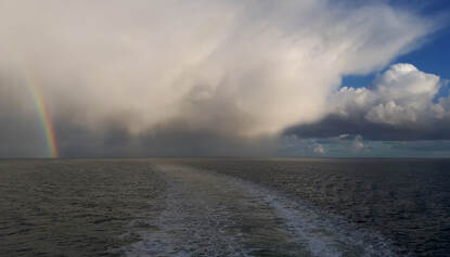 Regengebied met regenboog boven de Waddenzee tussen Harlingen en Terschelling