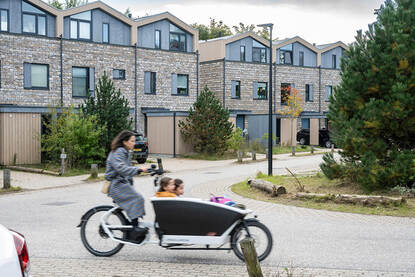 Vrouw fietst met een bakfiets met twee kinderen door een woonwijk.