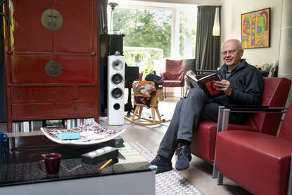Jan van den Heuvel zit in zijn woonkamer op de bank en leest een boek