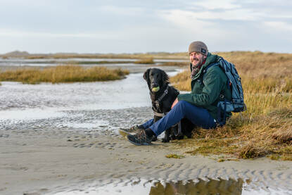 Adriaan Brouwer zittend op het strand van Terschelling met zijn zwarte hond.