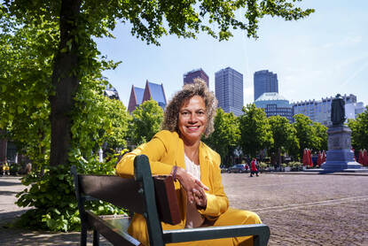 Bianca Maasdamme op een bankje met op de achtergrond de skyline van Den Haag