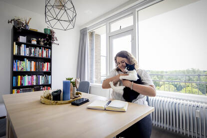 Annika Veenstra aan de keukentafel met een zwart-witte kat in haar armen