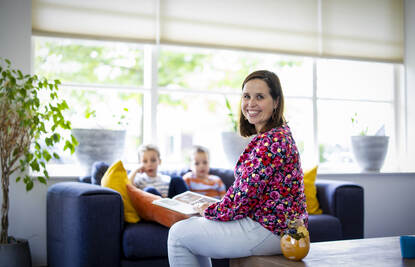 Danielle Willemse zittend op de salontafel met een boek in haar handen en twee kinderen op de achtergrond