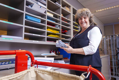 Jannie Beeloo staat met post in haar handen bij postvakjes met naast haar een postkar.