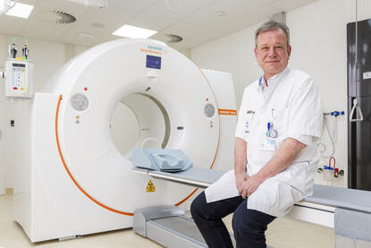 Wim zit in zijn doktersjas op het bed van een MRI-apparaat