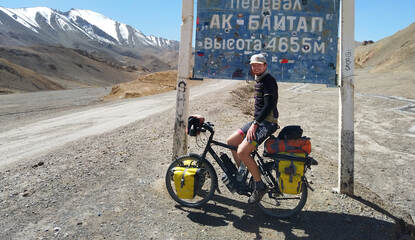 Richard zit op zijn fiets voor een buitenlands routebord midden in de bergen